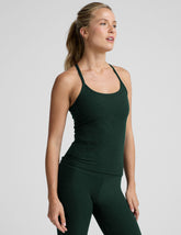 woman wearing a green tank top and leggings on a light gray background.